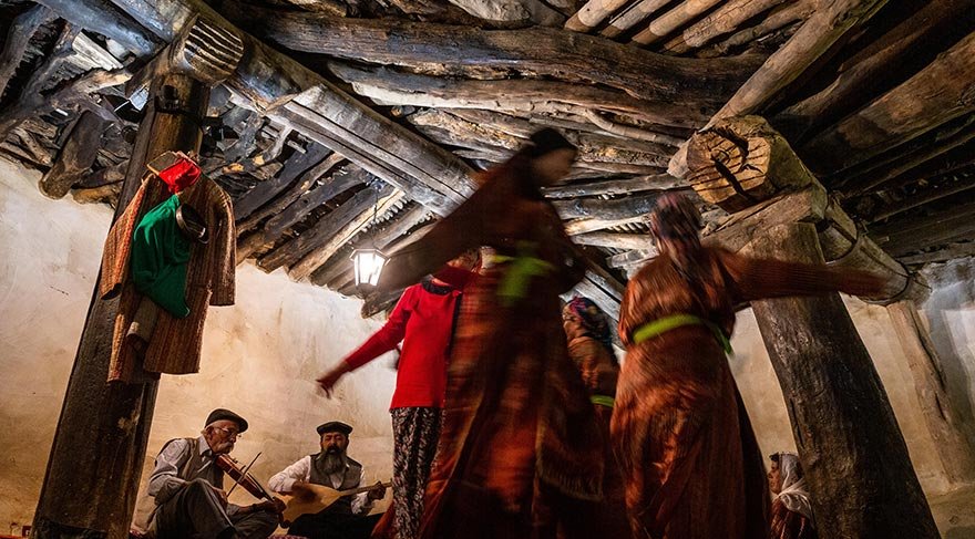 Twee mensen in het cemhuis maken muziek met snaarinstrumenten terwijl enkele anderen dansen op de muziek.