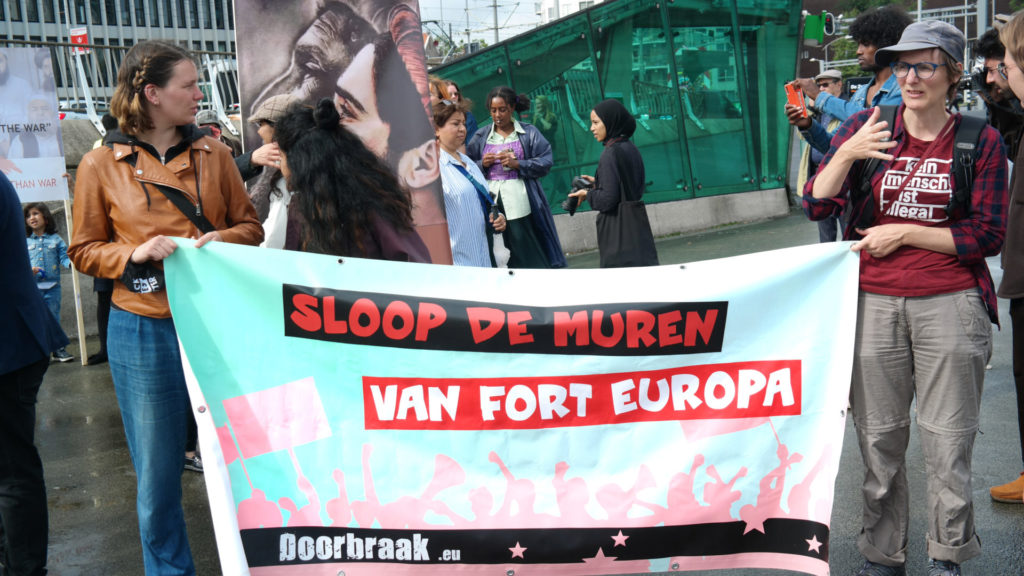 Twee demonstranten met een Doorbraak-spandoek met de tekst 'Sloop de muren van Fort Europa'.