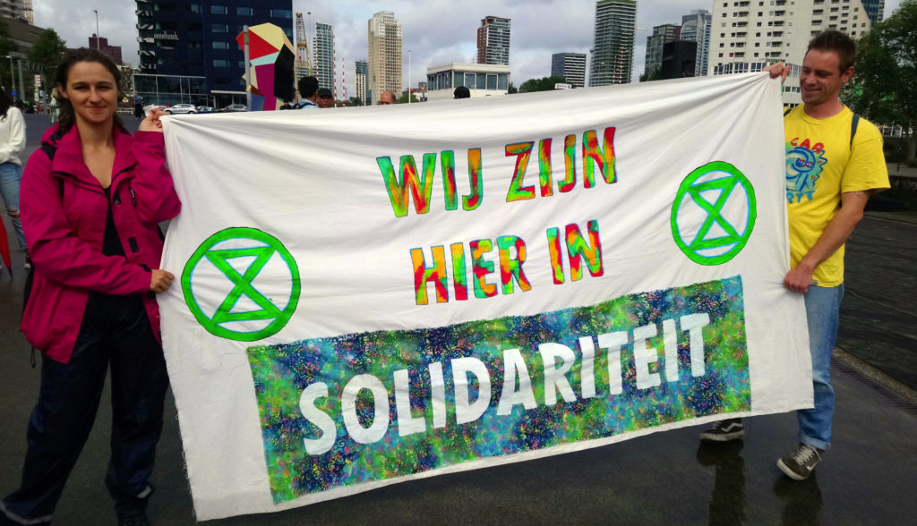 Kleurrijk spandoek van XR met de tekst 'Wij zijn hier in solidariteit'.