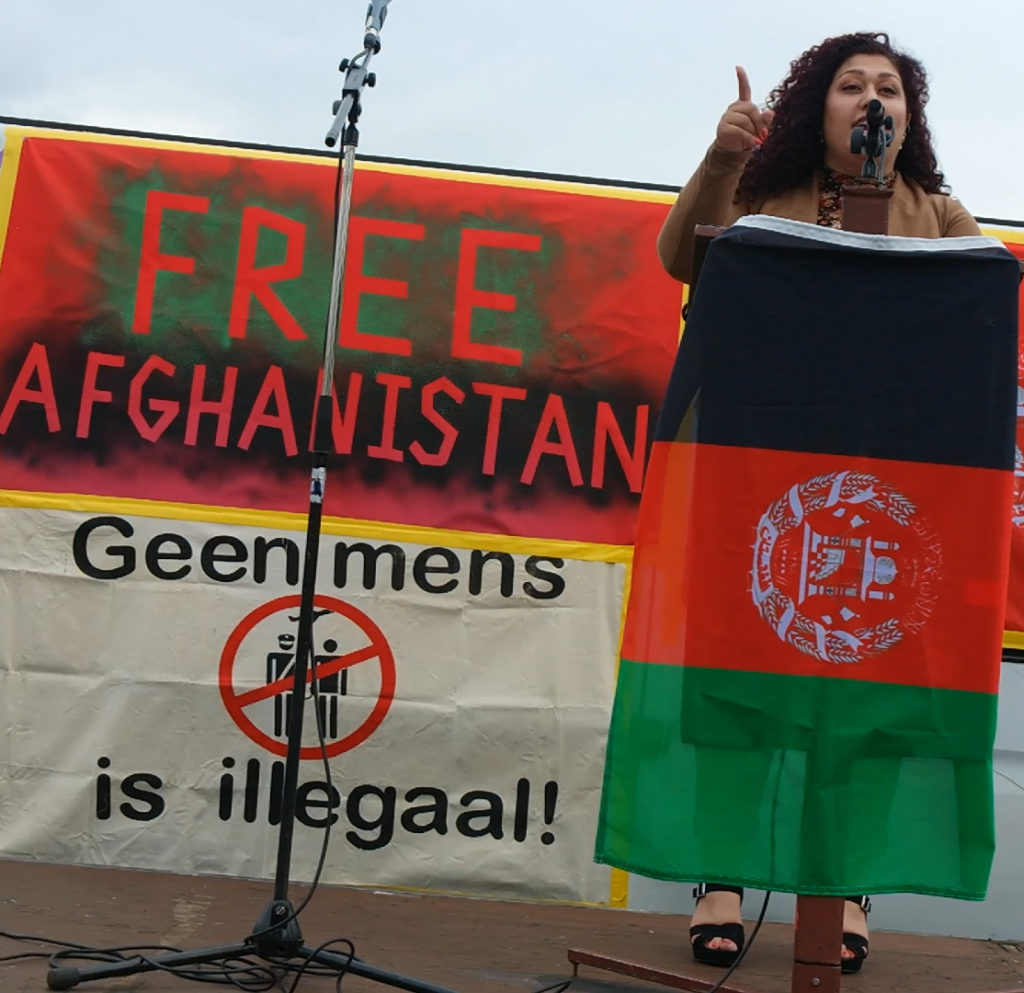 Arghawan op het podium achter de lessenaar met de Afghaanse vlag eraan.