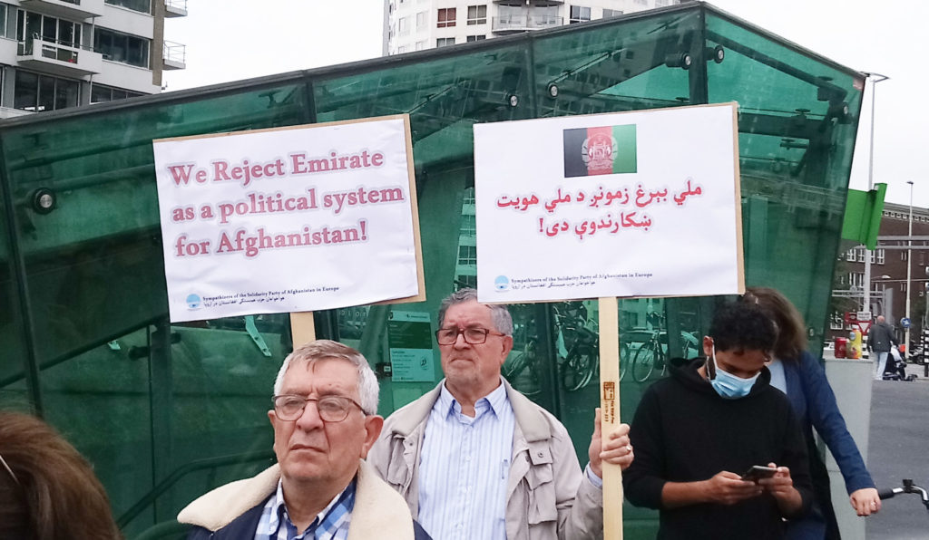 Twee oudere demonstranten, waarvan eentje met een bord met de tekst 'We reject Emirate as a political system for Afghanistan'. De andere draagt ook een bord, maar in een taal die ik niet kan lezen.