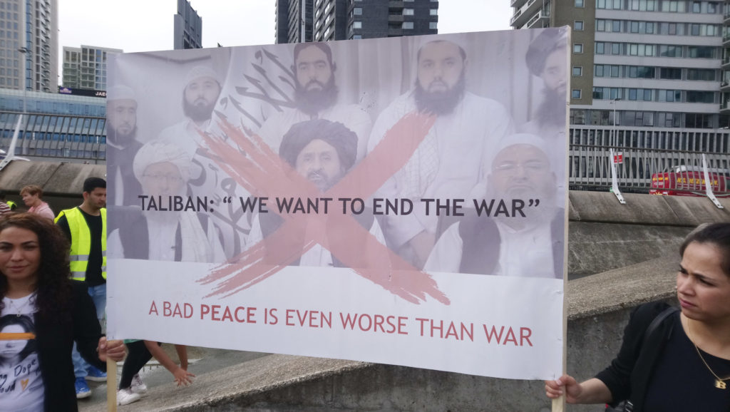Een spandoek met een foto van Taliban-kopstukken met een groot rood kruis erdoor en de tekst 'Taliban: "We want to end the war". A bad peace is even worse than war.'