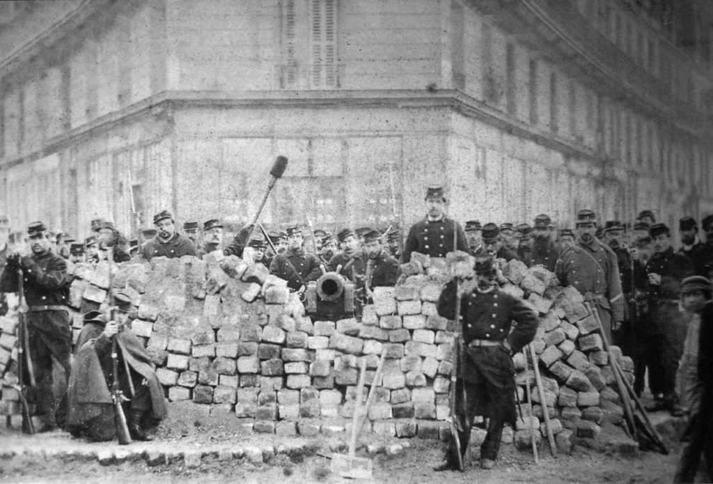 Zwart/wit foto van een barricade met een kanon met leden van de Nationale Garde eromheen.