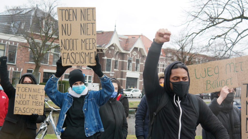 Demonstranten bij een Leids protest tegen Baudet. Ze hebben hun vuist in de lucht. Op kartonnen borden staat te lezen "Toen niet, nu niet, nooit meer fascisme" en "Weg met Baudet".