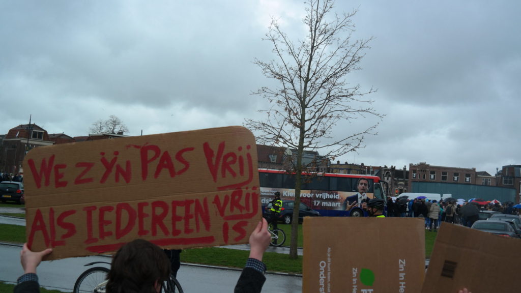 Iemand houdt een spandoek vast met de tekst "We zijn pas vrij als iedereen vrij is".