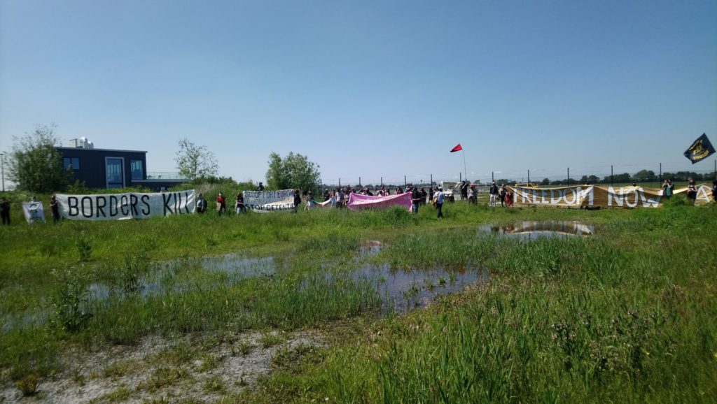 De deelnemers gezien vanaf de andere kan van een grasveld. Het is een grote groep mensen.