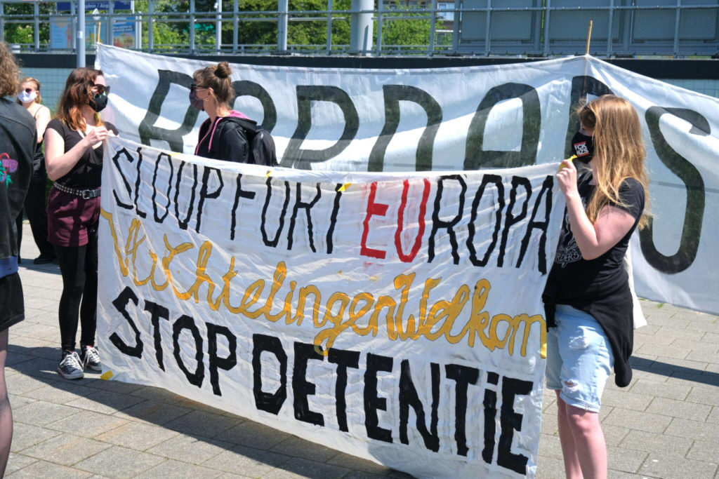 Demonstranten met een spandoek met de tekst "Sloop Fort Europa - vluchtelingen welkom - STOP DETENTIE".