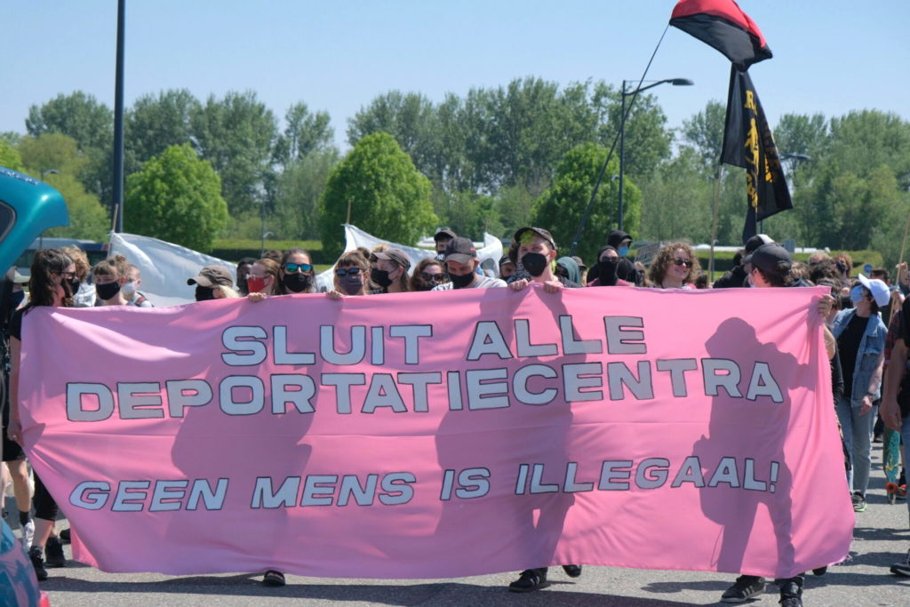 Groot roze spandoek met de tekst "Sluit alle deportatiecentra - geen mens is illegaal".