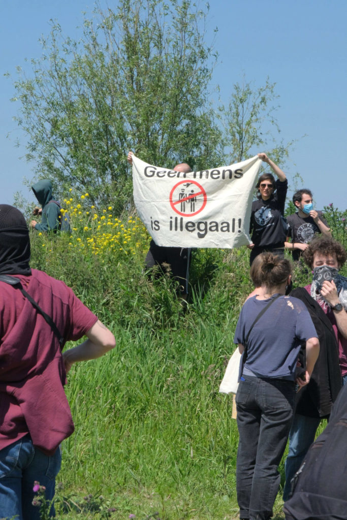 Mensen tussen het groen met een spandoek "Geen mens is illegaal!".