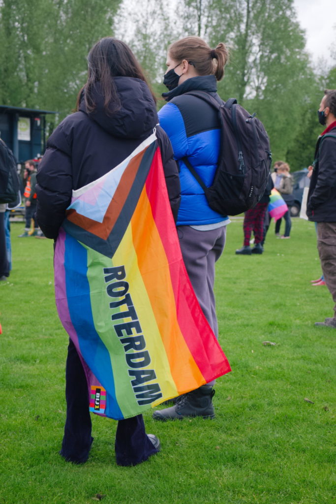 Iemand met om hun lijf een regenboogvlag met de tekst "Rotterdam" erop.