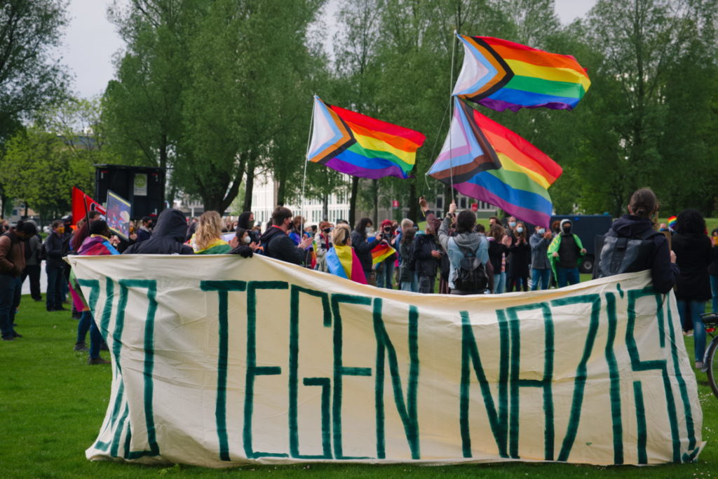 Groot spandoek "010 tegen nazi's!". Op de achtergrond veel regenboogvlaggen.