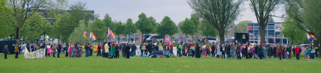 Breedbeeldfoto met een overzicht van de demo. Veel regenboogvlaggen.