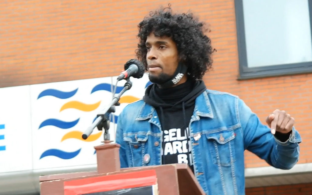 Daryll Landbrug achter de microfoon. Hij wijst met een vinger naar beneden.