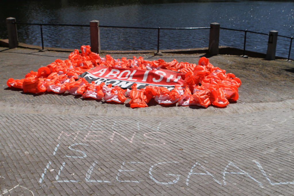 De zwemvesten met het spandoek op de kade, met op de stoep in krijt de tekst "Geen mens is illegaal".