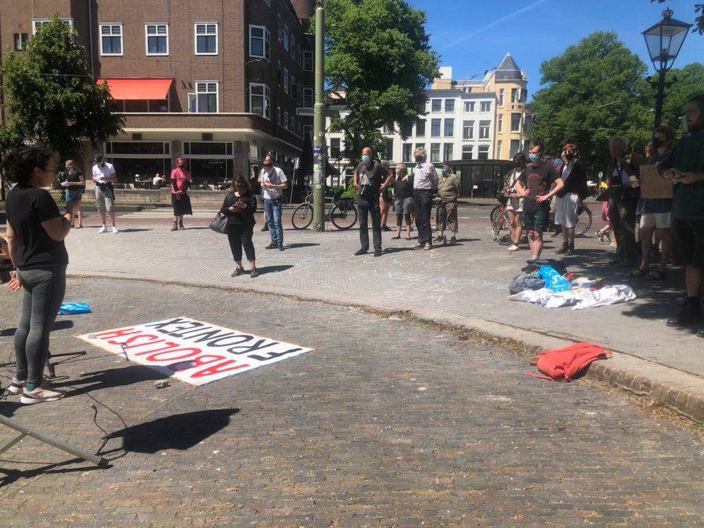 Een spreker staat achter een op de grond liggend spandoek met de tekst "Abolish Frontex".