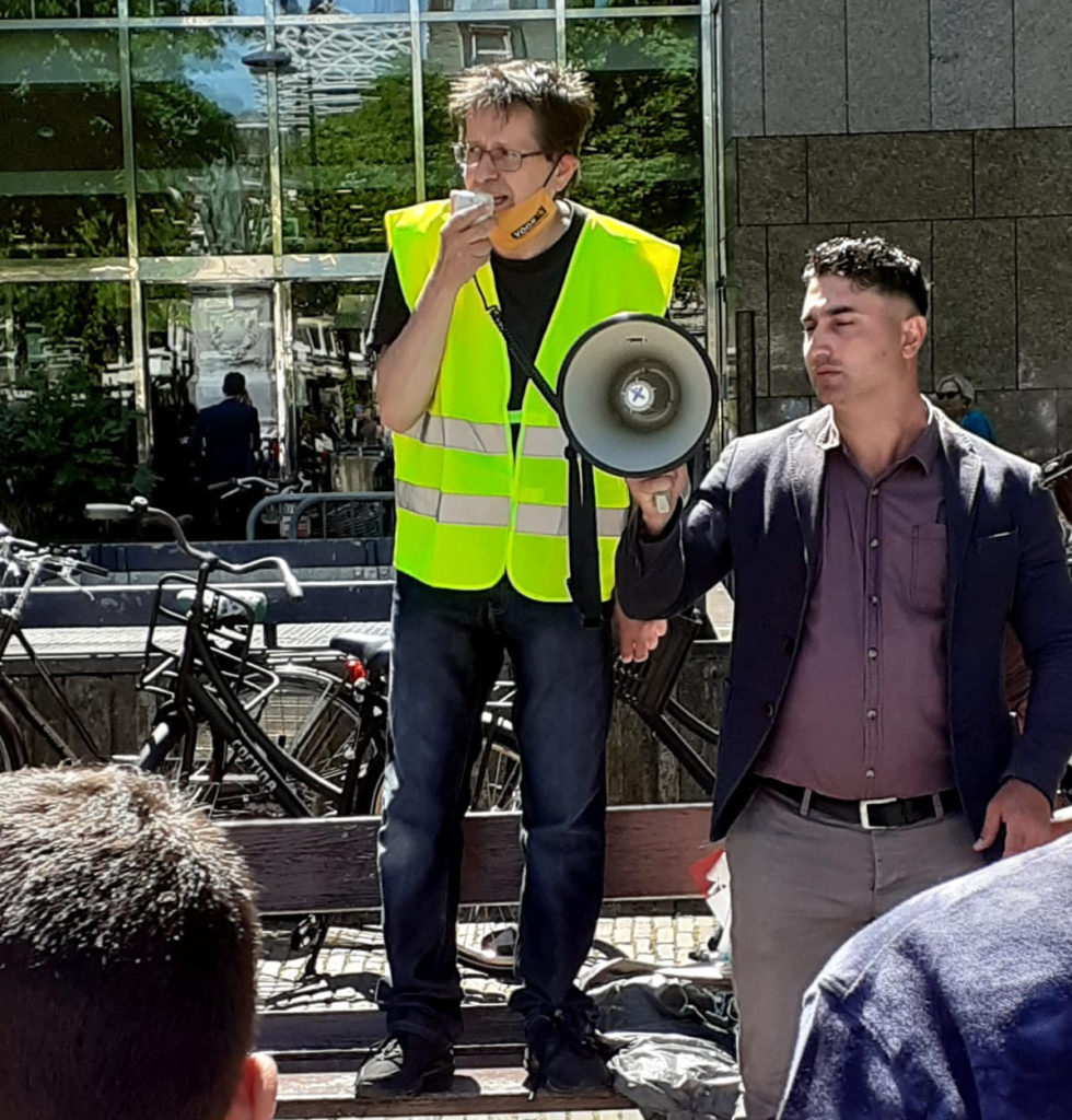 Eén van de sprekers voert het woord terwijl iemand naast hem de megafoon vasthoudt.