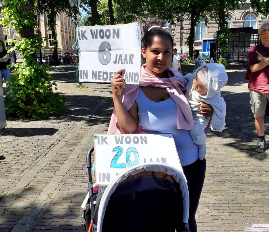 Iemand met een kindje op de arm draagt een bord "Ik woon 6 jaar in Nederland".