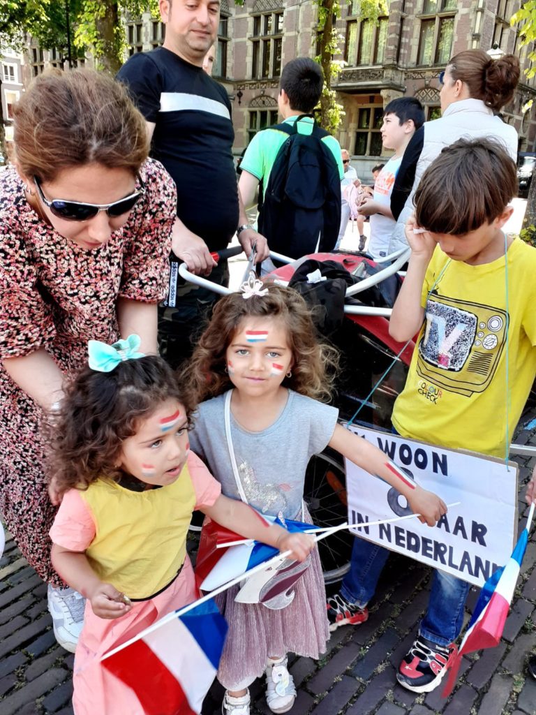 Twee kinderen met op hun gezichten en armen schmink in de kleur van de Nederlandse vlag en met Nederlandse vlaggen in hun handen.