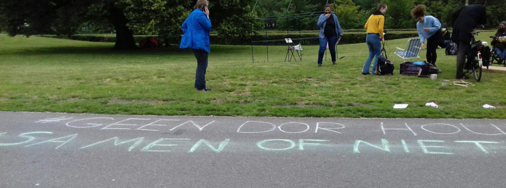 Op de voorgrond asfalt met daarop een gekrijte tekst: "Geen dor hout - Samen of niet". Op de achtergrond een aantal activisten in het gras.