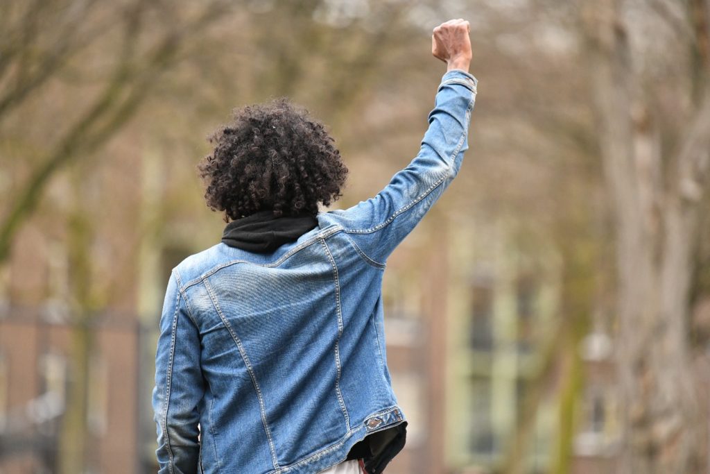 Daryll Landbrug met een spijkerjack aan en zijn rechtervuist in de lucht. We zien hem vanaf de achterzijde.