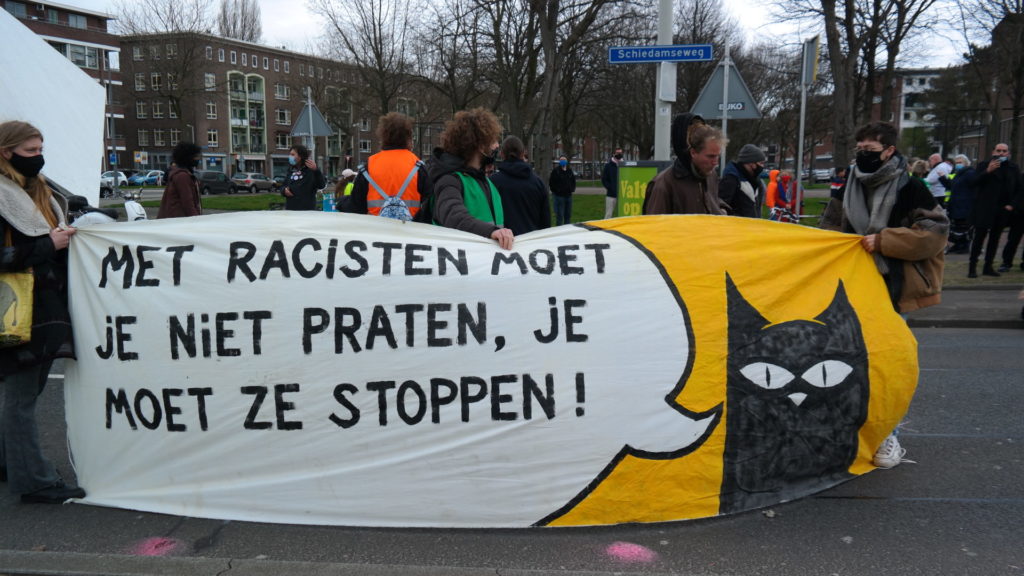 Spandoek met een zwarte kat met een tekstballon met daarin de tekst "Met racisten moet je niet praten, je moet ze stoppen!".