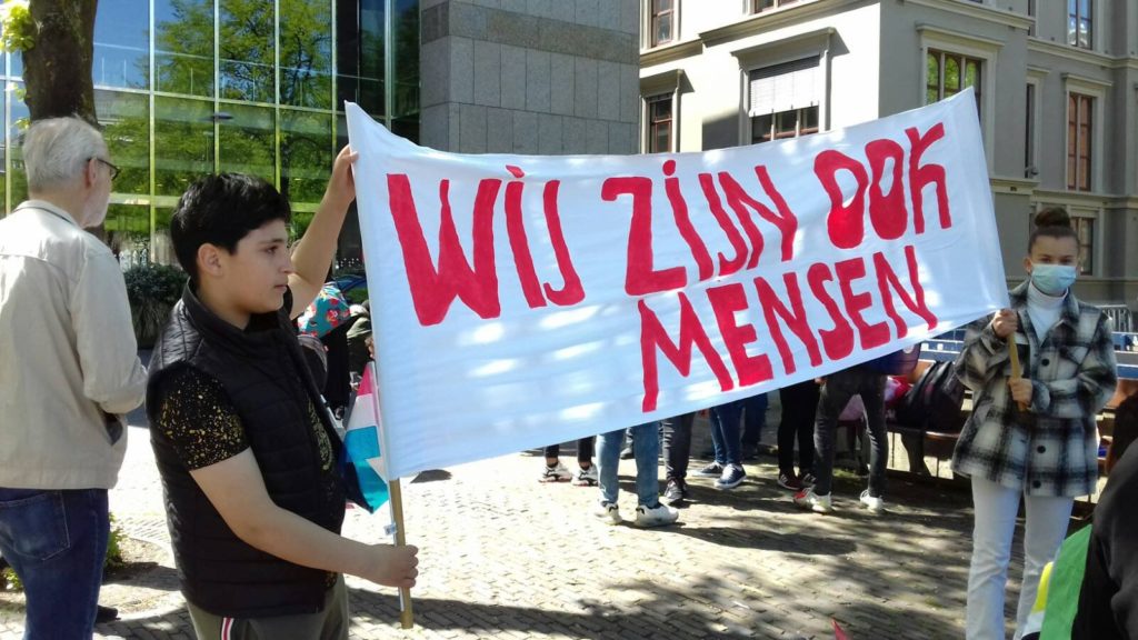 Twee jonge demonstranten met een spandoek met de tekst: "Wij zijn ook mensen".