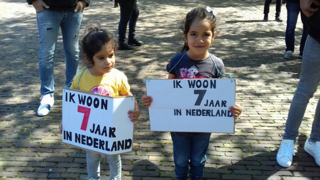 Twee kinderen met elk bordjes waar op staat dat ze al zeven jaar (hun hele leven?) in Nederland zijn.