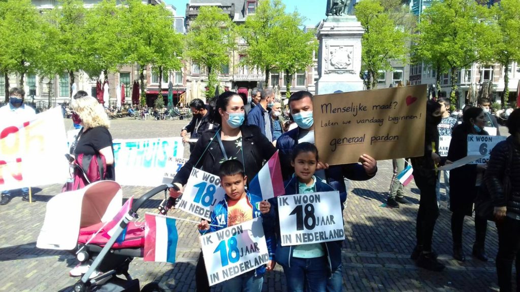 Een gezin bij de demonstratie, ze dragen een bord met de tekst: "Menselijke maat? Laten we vandaag beginnen! Generaal pardon."