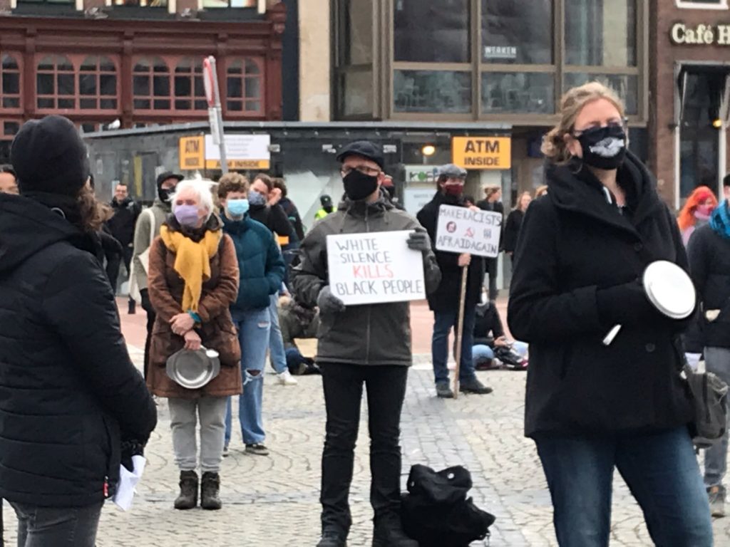 Mensen op de Grote Markt in Groningen. In het midden een witte man met een pet en een bord met de tekst "White silence kills black people".