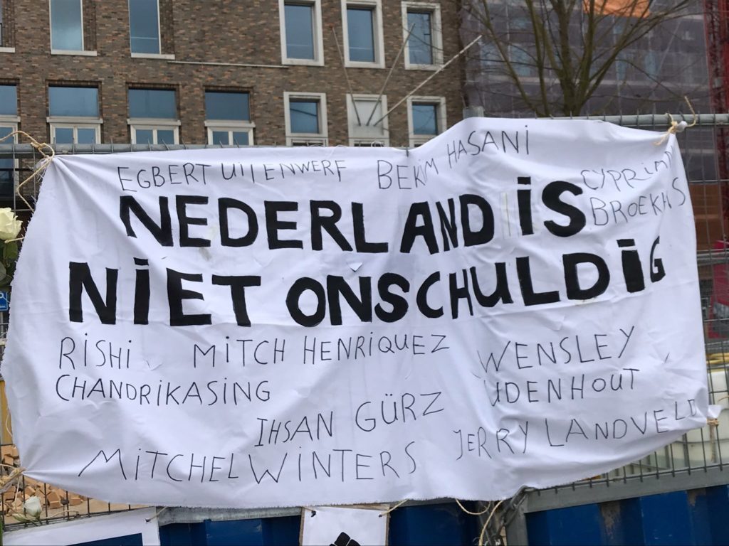 Een close-up van het spandoek met namen van slachtoffers van politiegeweld in Nederland. De namen die zichtbaar zijn op de foto: Cyprian Broekhuis, Rishi Chandrikasing, Mitch Henriquez, Ihsan Gürz, Wensley Udenhout, Mitchel Winters, Jerry Landveld.