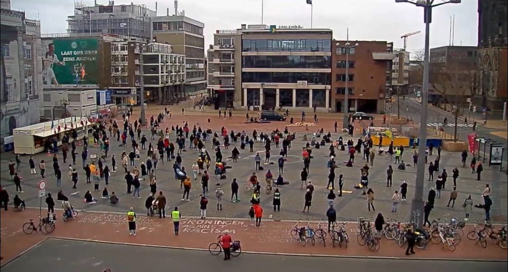 Overzicht van het protest in Groningen, van een afstand en vanuit een hoge positie genomen. Je ziet tientallen mensen die gelijkmatig verspreid staan.