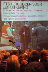 Wandprojectie met de sprekers en daaronder dwangarbeiders.