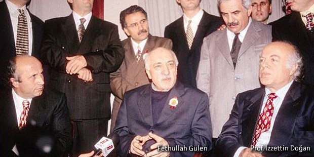Foto met op de voorgrond Fethullah Gülen in een donkerblauw pak met een insigne op het revers, naast hem Prof. Izzettin Doğan in een donkerblauw pak en een rode stropdas. Op de achtergrond nog veel meer mannen in ouderwetse 'nette' pakken.