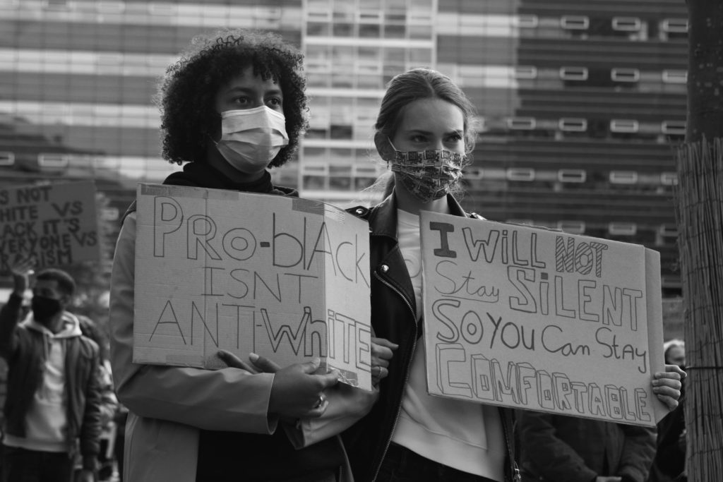 Demonstranten met kartonnen borden. Teksten: "Pro-Black isn't anti-white" en "I will not stay silent so you can stay comfortable".