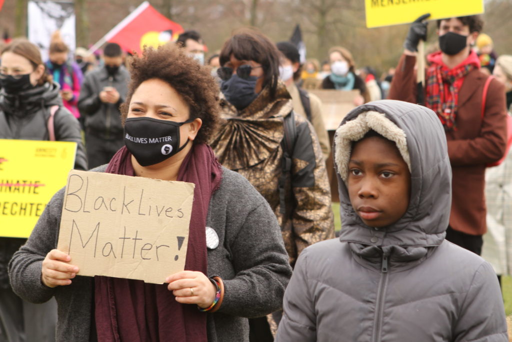 Een zwart kind en een zwarte volwassene naast elkaar. Het kind kijkt ernstig. De volwassene draagt een bord met de tekst "Black lives matter".