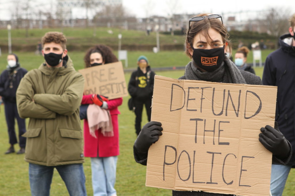 Een persoon met een bord met de tekst "Defund the police".