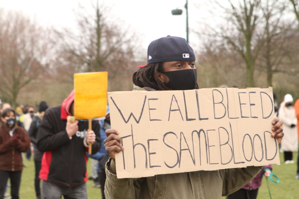 Een persoon met een bord met de tekst "We all bleed the same blood".