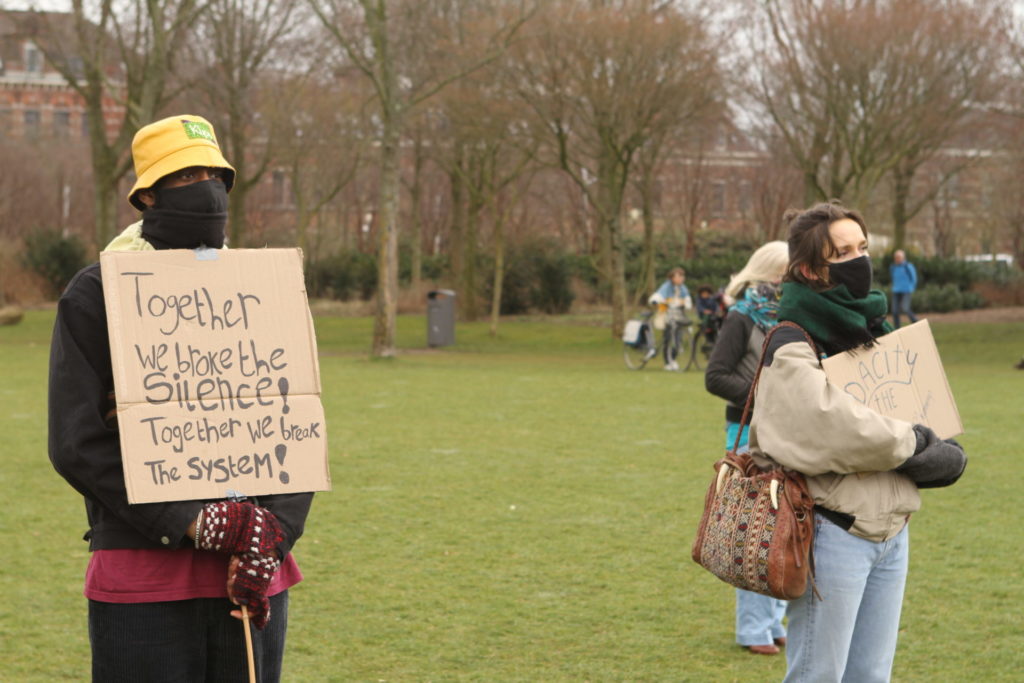 Twee personen waarvan eentje met een bord met de tekst "Together we broke the silence! Together we break the system!".