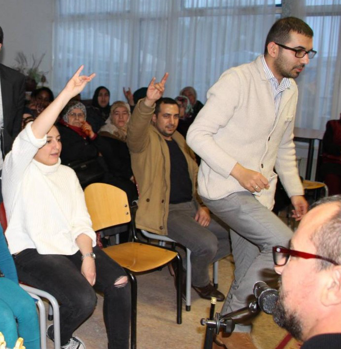 Een groep mensen in een publiek brengen de grijze wolven groet. Onder hen zijn Halil Koçak en Alperen Doruk.