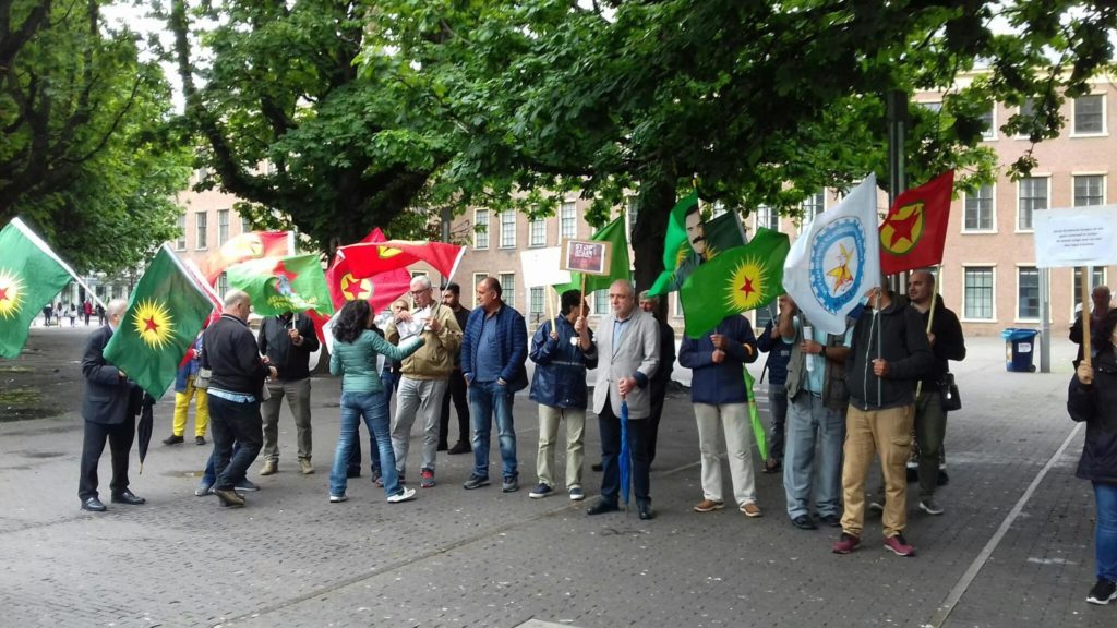 Een deel van de demonstranten staat op het plein onder de grote bomen. Veel vlaggen.