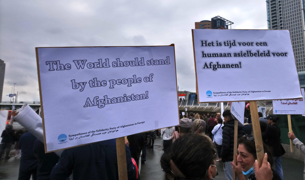 Twee borden, teksten: 'The world should stand by the people of Afghanistan' en 'Het is tijd voor een humaan asielbeleid voor Afghanen!'.