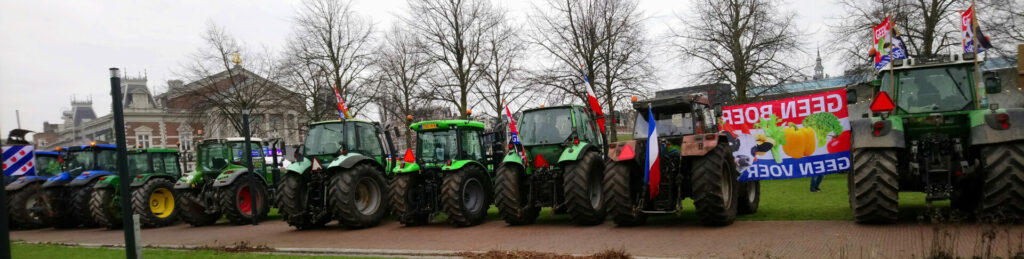 Een rij tractoren op het museumplein. Veel zijn met Nederlandse vlaggen uitgerust, en 1 met een Friese vlag. Tussen twee tractoren hangt een spandoek met de tekst 'geen boer, geen voer'.