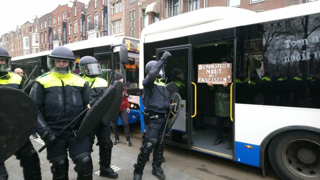 M.E.-ers drijven de antifascistische demonstranten de bussen in.