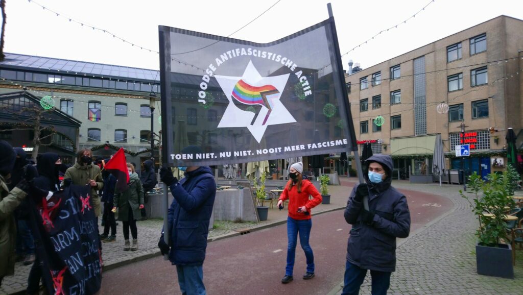 Twee antifascistische demonstranten houden een spandoek op met de tekst 'Joodse antifascistische actie. toen niet. nu niet. nooit meer fascisme'.