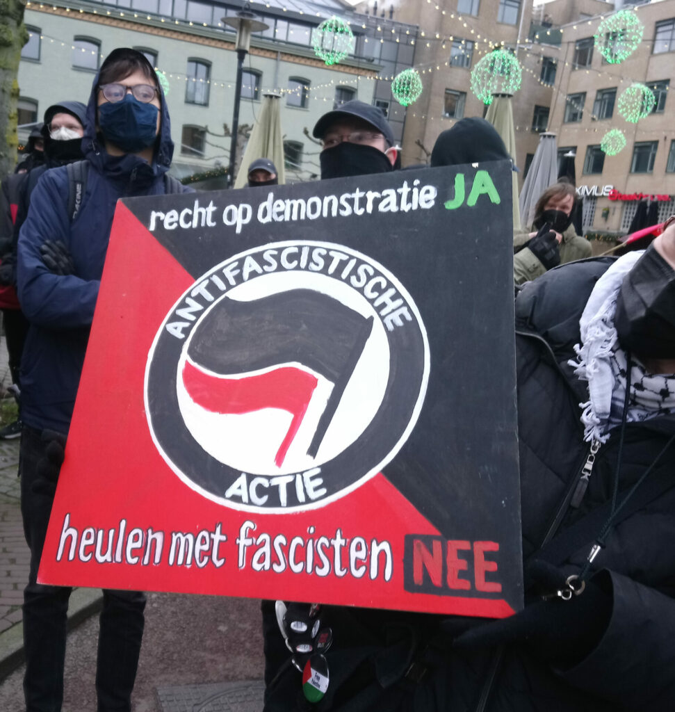 In zwart geklede demonstranten tonen een antifascistisch protestbord met de tekst 'recht op demonstratie ja, heulen met fascisten nee'.