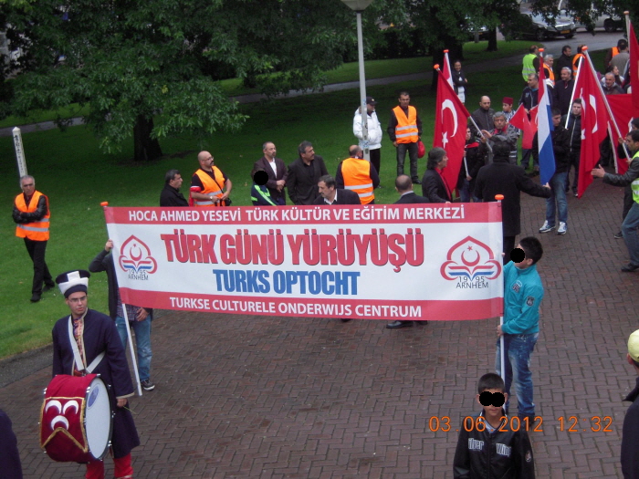 Spandoek tijdens de optocht van 2012 waaruit duidelijk wordt dat de organisatie in handen is van de vereniging Hoca Ahmed Yesevi. Op de trommel zien we de MHP-vlag met de drie halve manen.