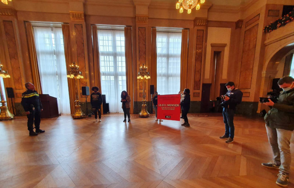 Overzicht van een deel van de mensen in de Burgerzaal van het stadhuis. Diverse journalisten zijn aanwezig. De zaal is groot en statig, met een parketvloer en marmeren wanden.