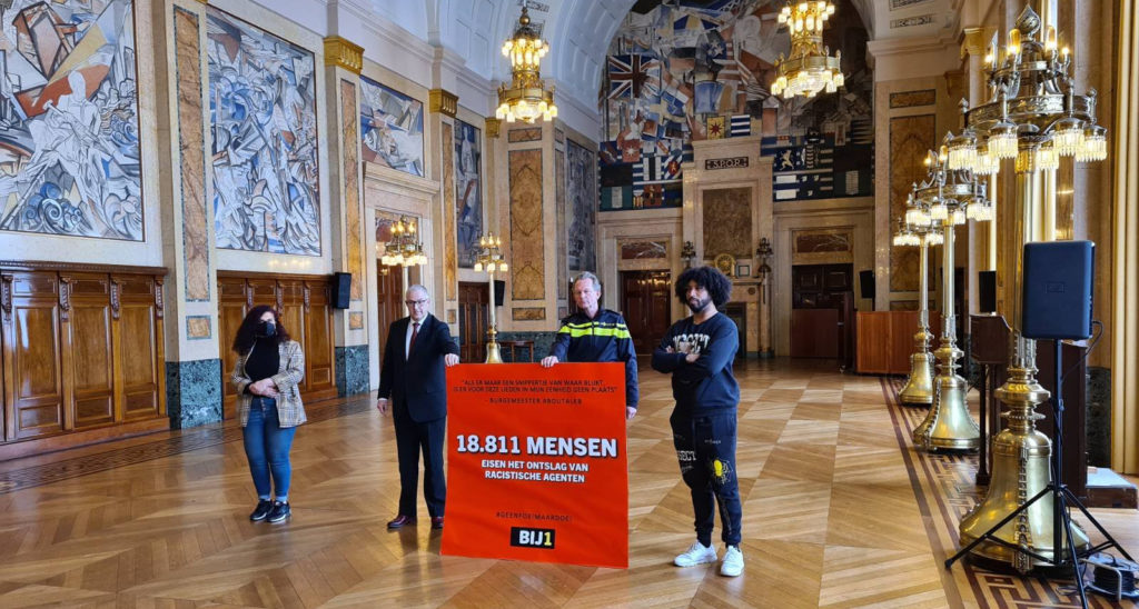 De burgemeester en de politiebaas houden met frisse tegenzin de rode kaart vast voor de foto. Dean Bowen en Sandra Salome staan aan weerszijden.