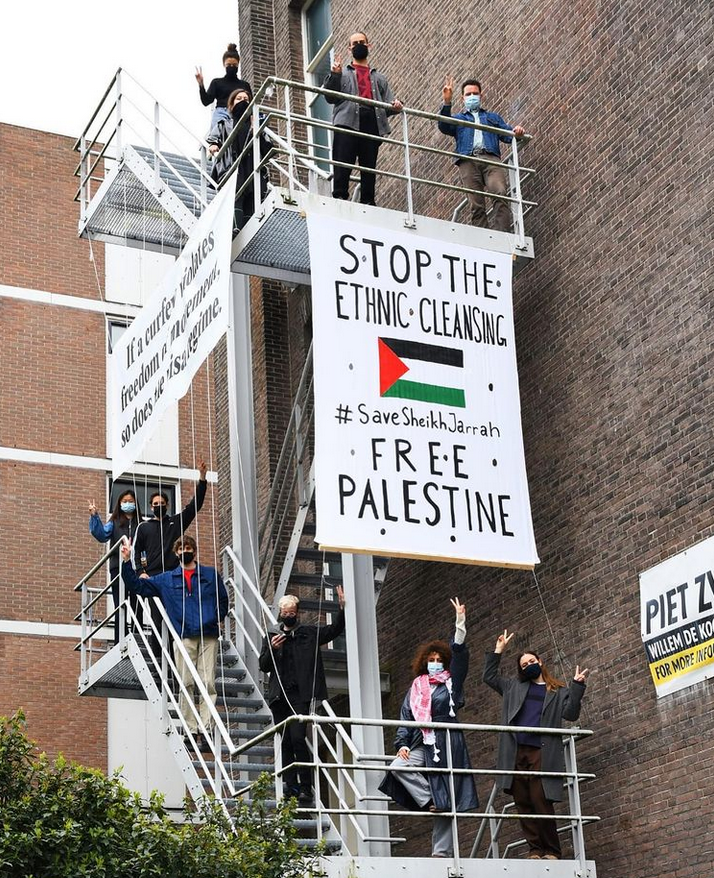 Brandtrappen met daarop een aantal mensen en een groot spandoek met de tekst "Stop the ethnic cleansing / #SaveSheikhJarrah / Free Palestine". Op de zijkant van de brandtrap zit ook een spandoek maar dat is niet goed leesbaar.