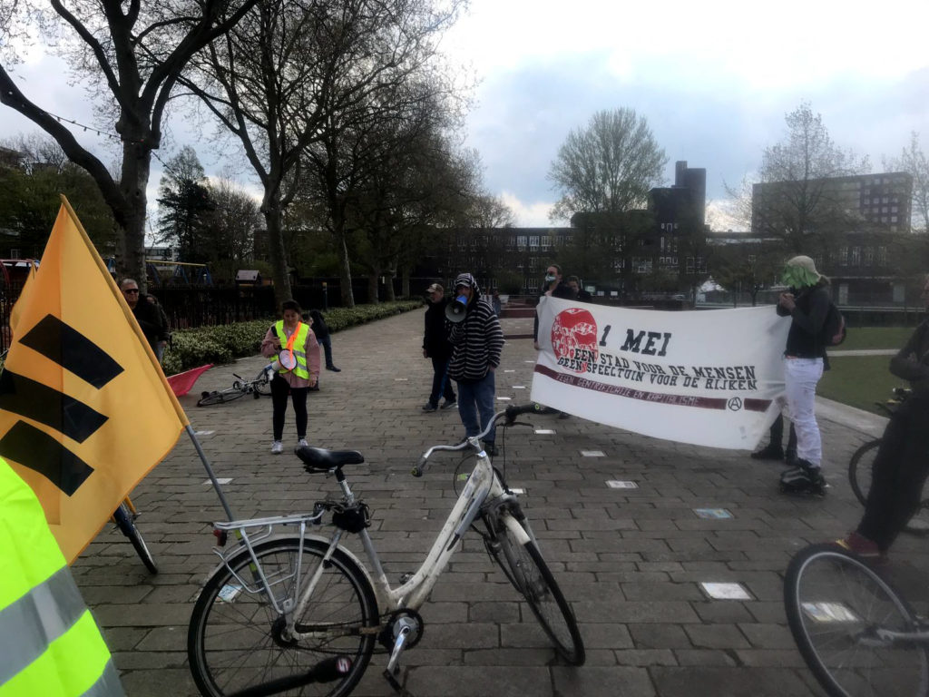 Demonstranten met een spandoek waar op staat "1 mei - een stad voor de mensen, geen speeltuin voor de rijken".